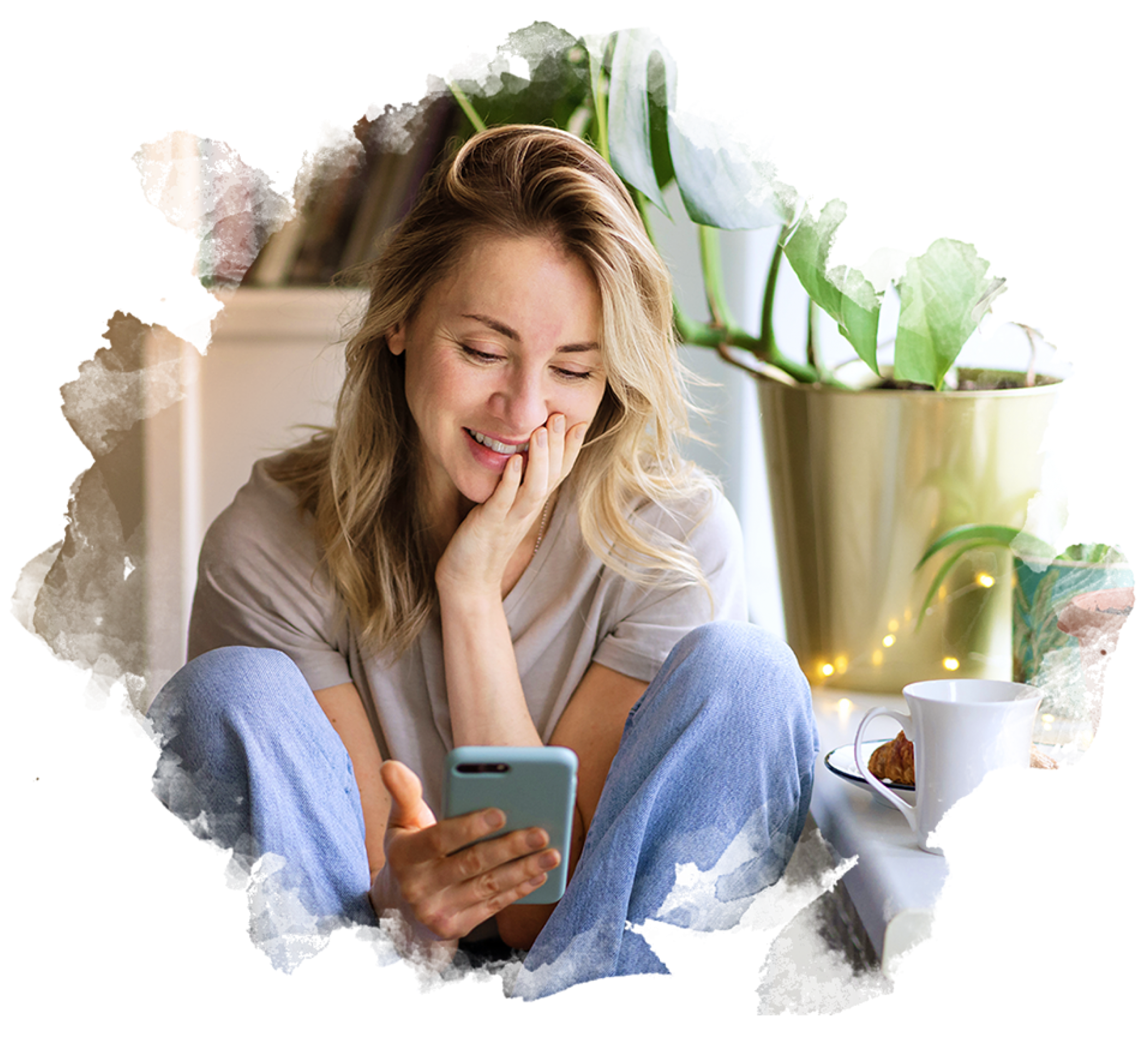 Kvinde i afslappet tøj sidder med mobiltelefon ved sofabord med kaffekop og grøn plante.